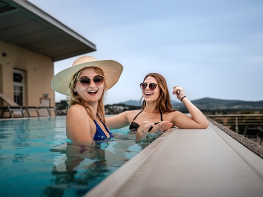 Ab ins Wellnesshotel in Bayern! Zwei Gäste entspannen mit Sommerhüten am Skypool des 4‑Sterne‑Superior Randsbergerhof in Cham, Bayerischer Wald